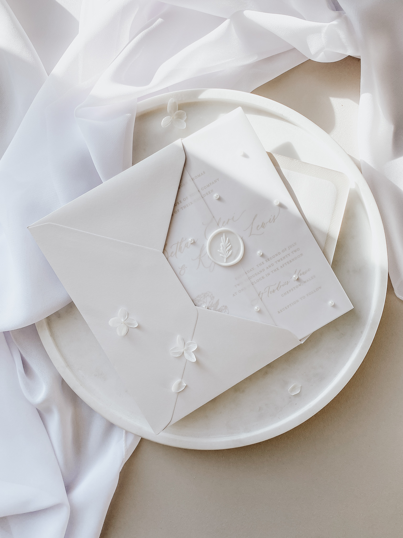 Elegant neutral wedding invitation wrapped in a vellum sleeve decorated with pearl embellishment.