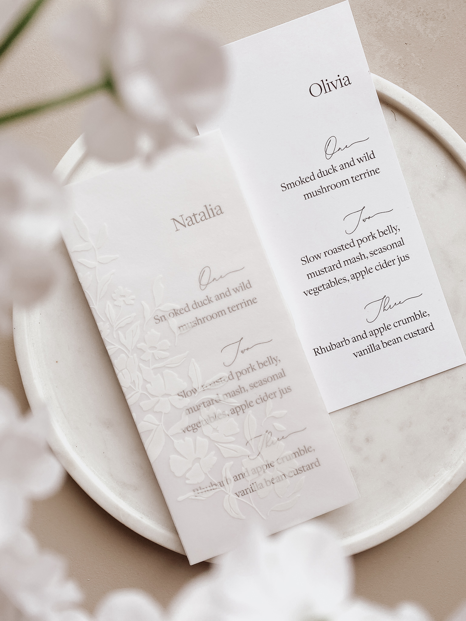 Modern wedding menu cards wrapped in a vellum sleeve decorated with white ink flowers.