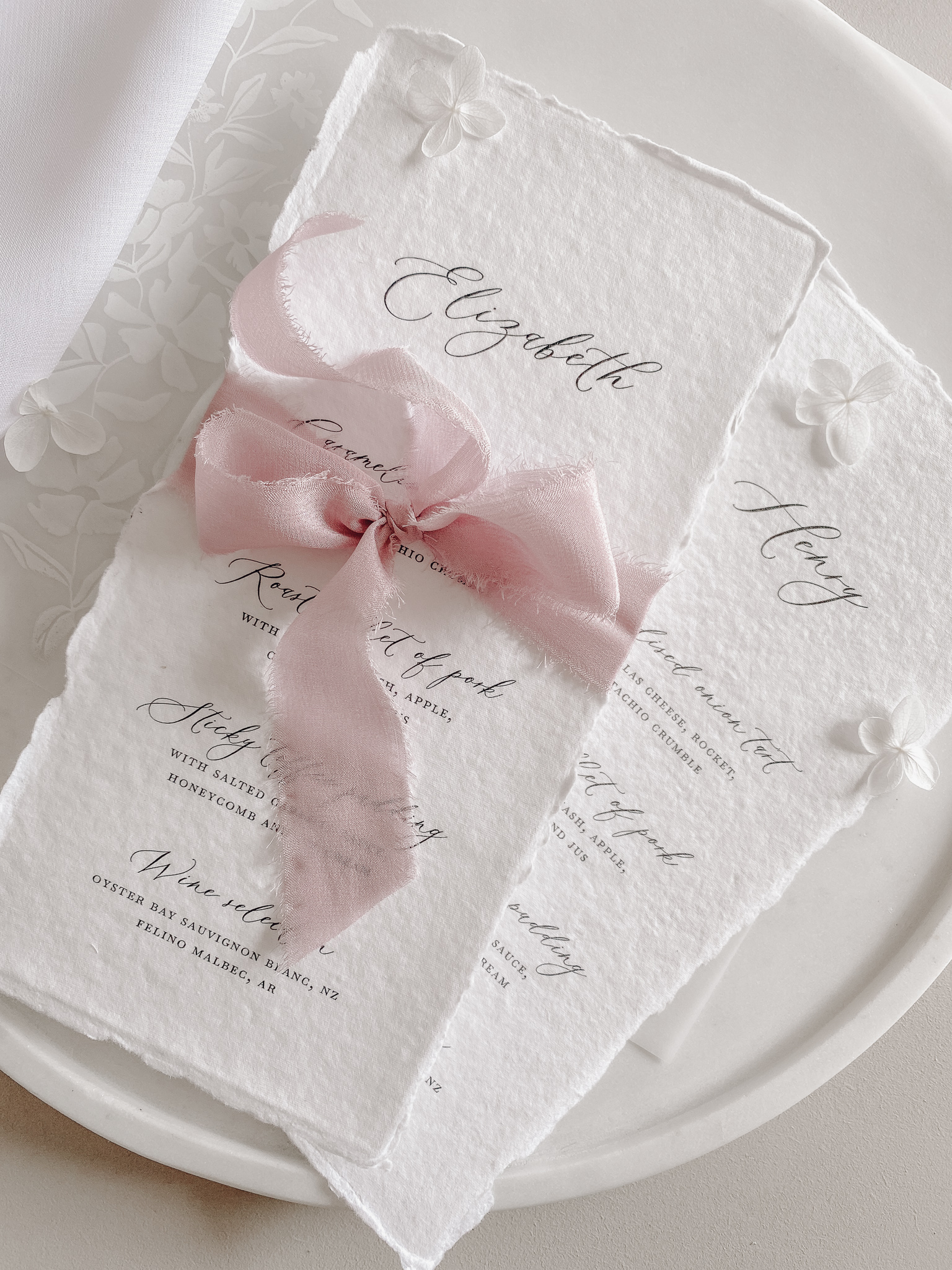 Handemade paper wedding menu cards with elegant calligraphy and tied with soft pink silk ribbon.